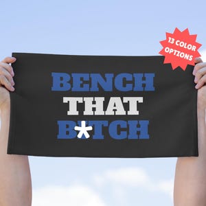 May include: Black rectangular towel with the text "BENCH THAT B*TCH" in blue and white block letters. A red starburst graphic in the upper right corner reads "13 COLOR OPTIONS".