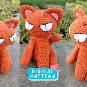 May include: A crocheted orange cat plush toy with white eyes and teeth. The cat has a stitched-on frown and pink ears. The toy is sitting on a grey surface. The text "DIGITAL PATTERN" is visible in the image.