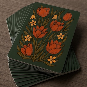 May include: A stack of playing cards with a floral design. The cards have a dark green background with orange tulips and yellow flowers. The cards are stacked on a wooden surface.