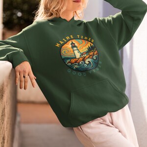 May include: A dark green hoodie with a front pocket and a hood. The hoodie features a circular graphic with a lighthouse, the words "MAINE TIDES" and "GOOD VIBES". The graphic has orange, blue, and green colors.