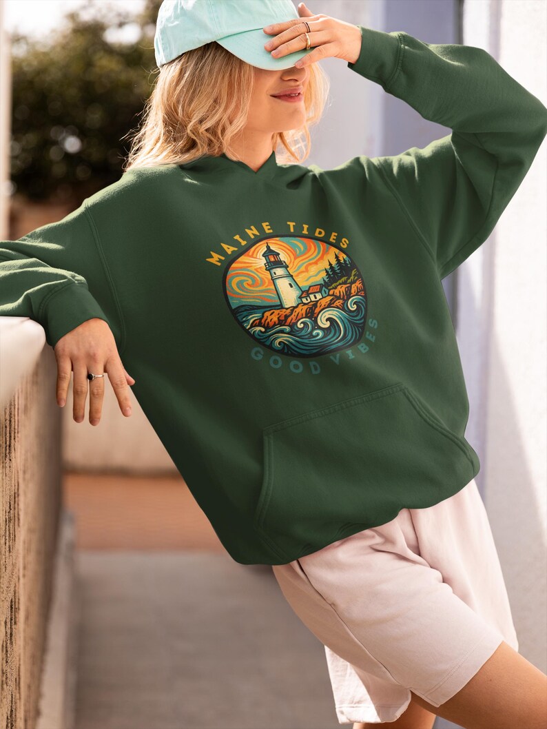 May include: A dark green hoodie with a front pocket and a hood. The hoodie features a circular graphic with a lighthouse, the words "MAINE TIDES" and "GOOD VIBES". The graphic has orange, blue, and green colors.