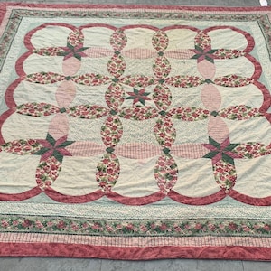May include: A large, handmade quilt with a repeating pattern of interlocking circles and floral starbursts. The quilt features a cream-colored background with red, pink, and green floral accents. The border is a mix of floral and solid red fabrics.