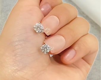 May include: A pair of sparkling, round-cut diamond stud earrings. The earrings are set in a silver metal, and are displayed against a neutral background. The earrings are a classic jewelry item.
