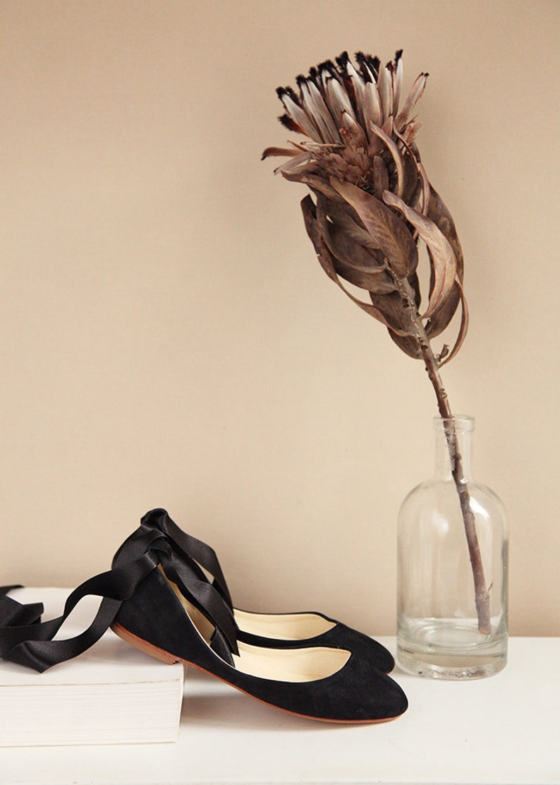 side view of pair of black nubuck ballet flats with satin ribbons with flower decoration