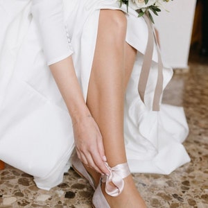 bride tying the satin ribbons on her ankle of a bridal ballerina shoe