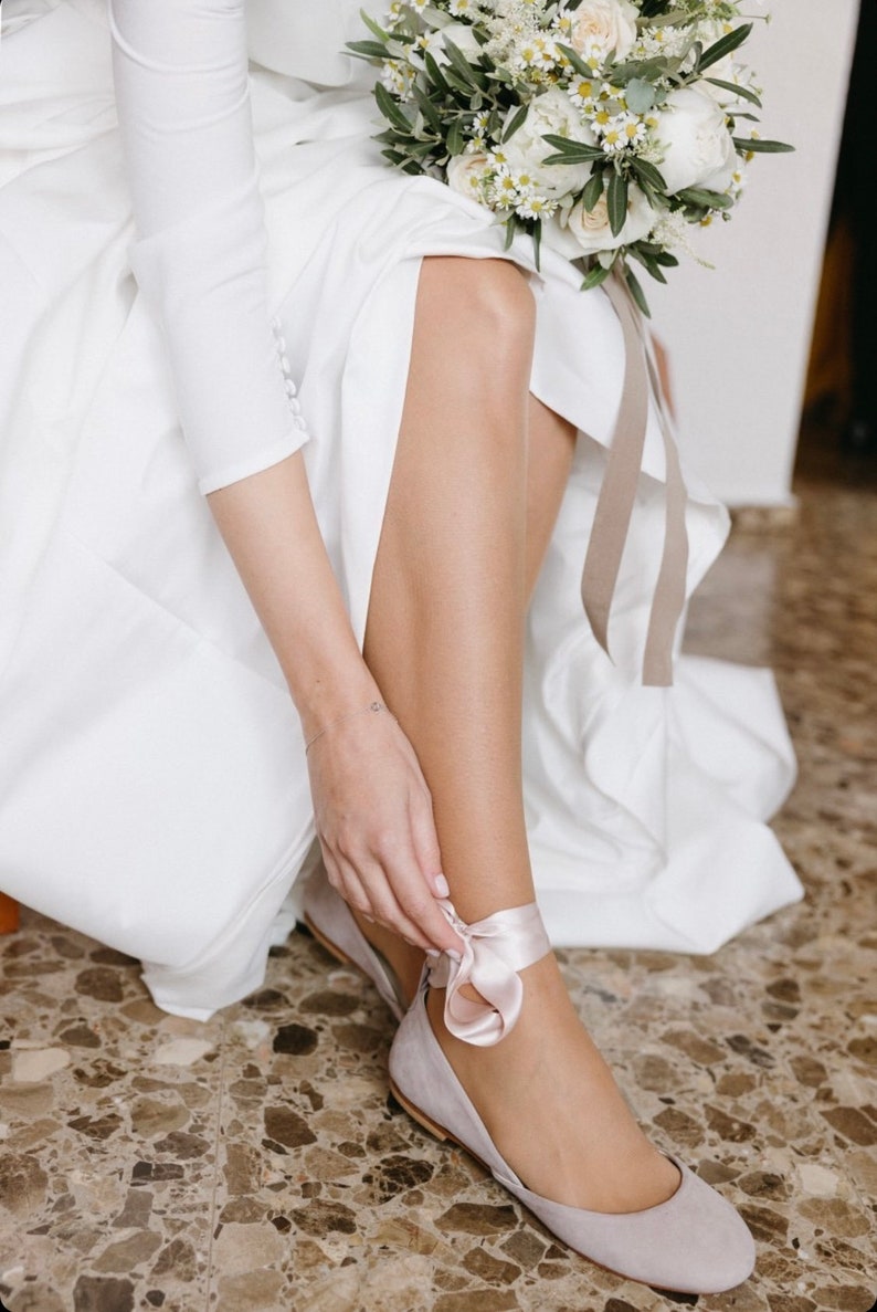 bride tying the satin ribbons on her ankle of a bridal ballerina shoe
