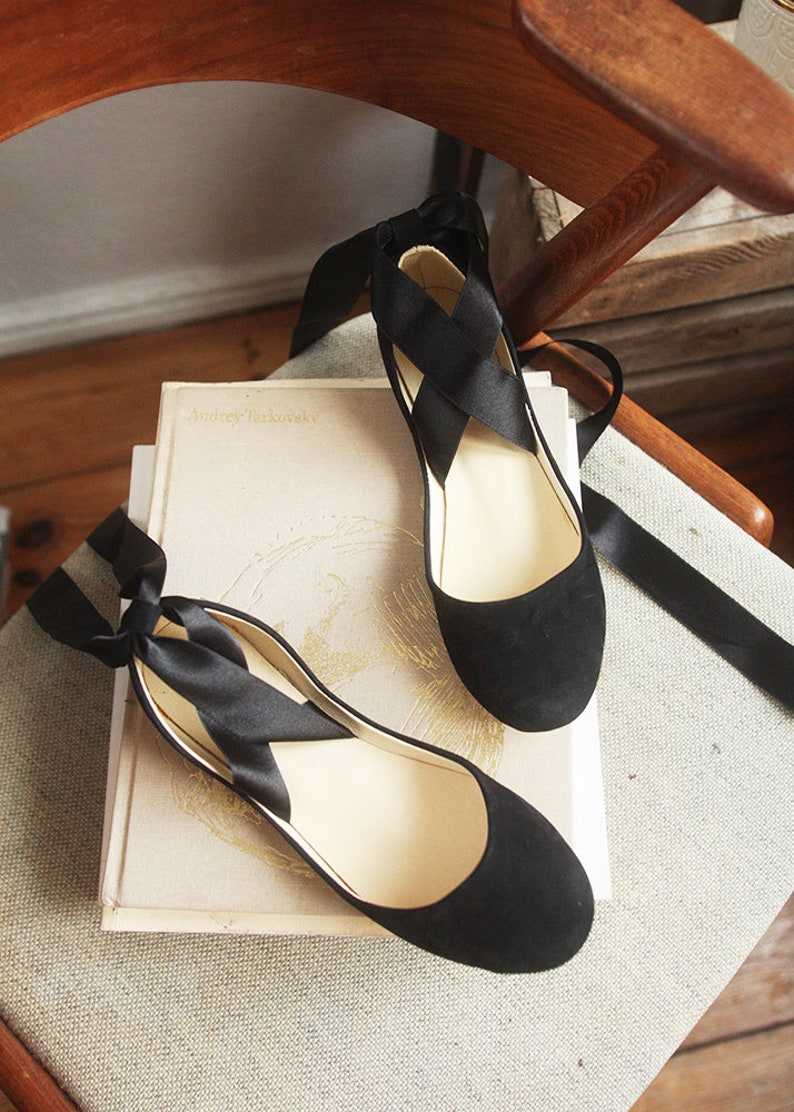 top view of a pair of black suede ballerinas with embedded long satin straps on a chair
