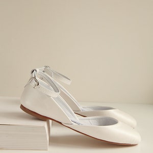 side view of a pair of pearl ivory wedding ballet flats with leather buckles inserted