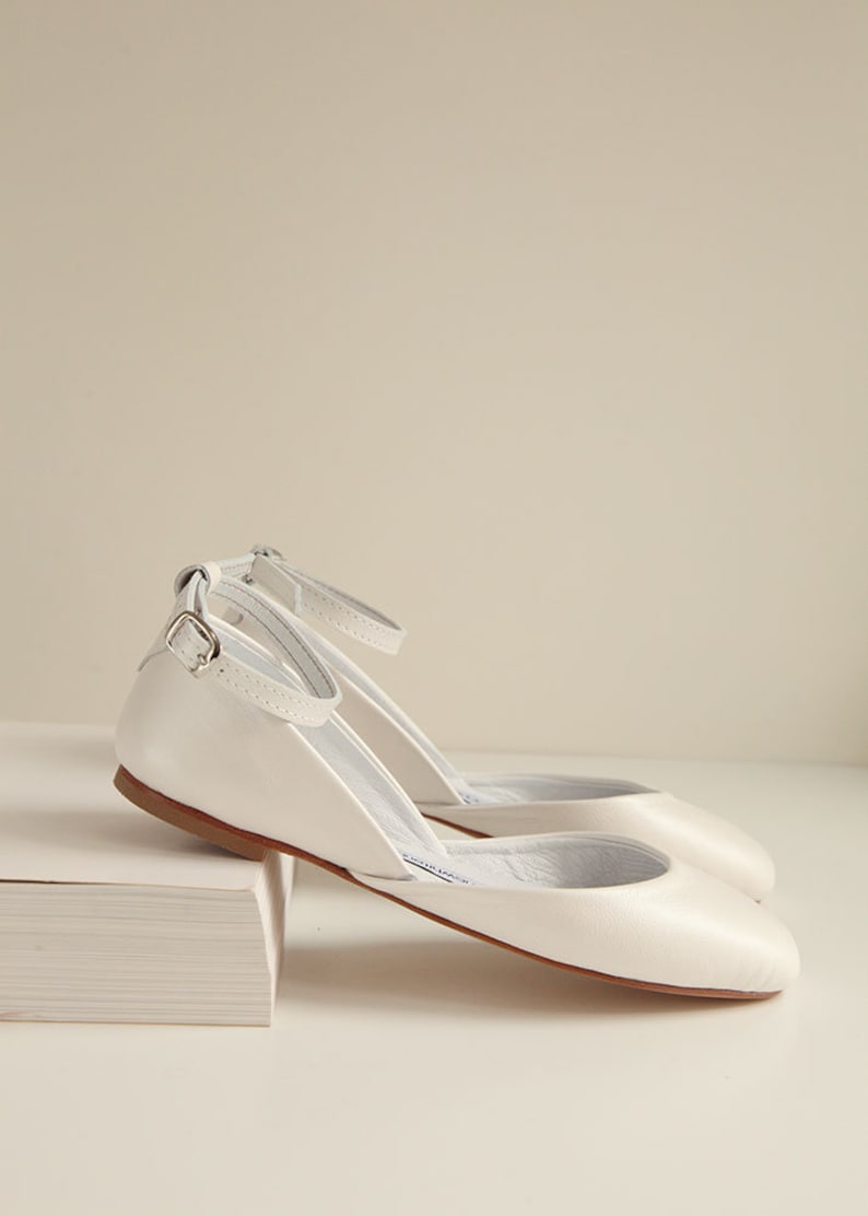 side view of a pair of pearl ivory wedding ballet flats with leather buckles inserted