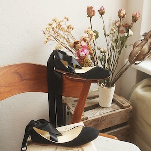 still image of flowers and a pair of black suede ballet flats with long satin ribbons