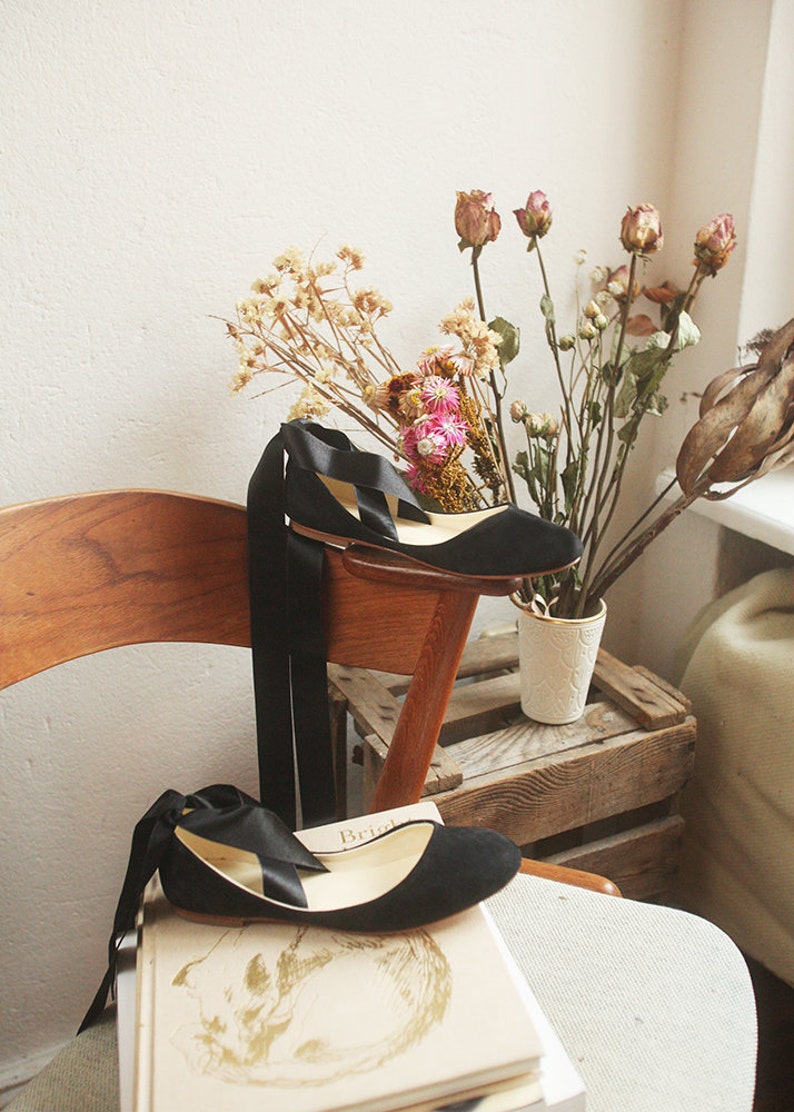 still image of flowers and a pair of black suede ballet flats with long satin ribbons