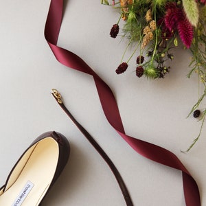 detailed photo of a bordeaux ballerina with matching leather strap and satin ribbon and flowers in the background