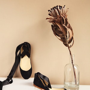 top and side show of a pair of black suede ballerinas with satin ribbons