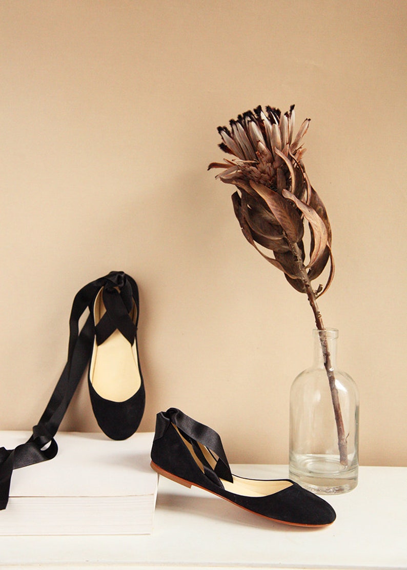 top and side show of a pair of black suede ballerinas with satin ribbons