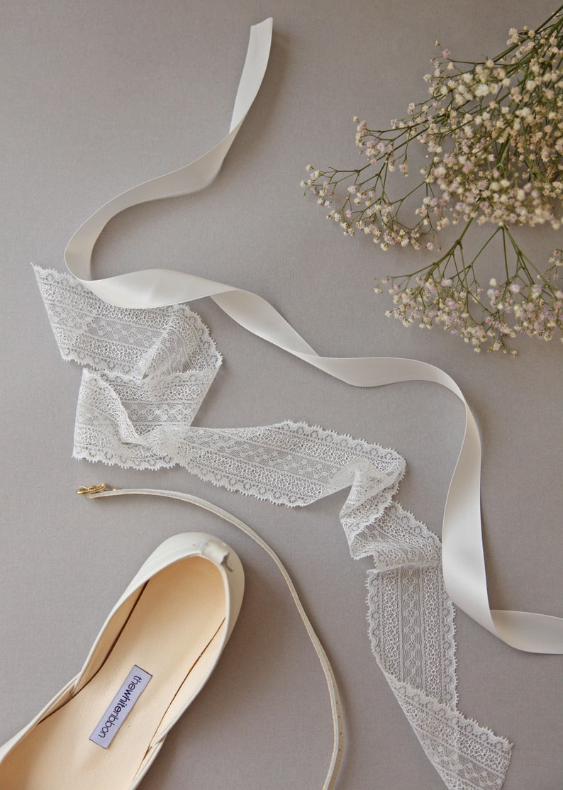 Detail shot from top of lace, satin ribbon and leather ankle strap with view of partial flower bouquet.