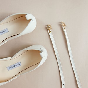 Detail shot of a pair of ankle straps with gold buckles on blush background