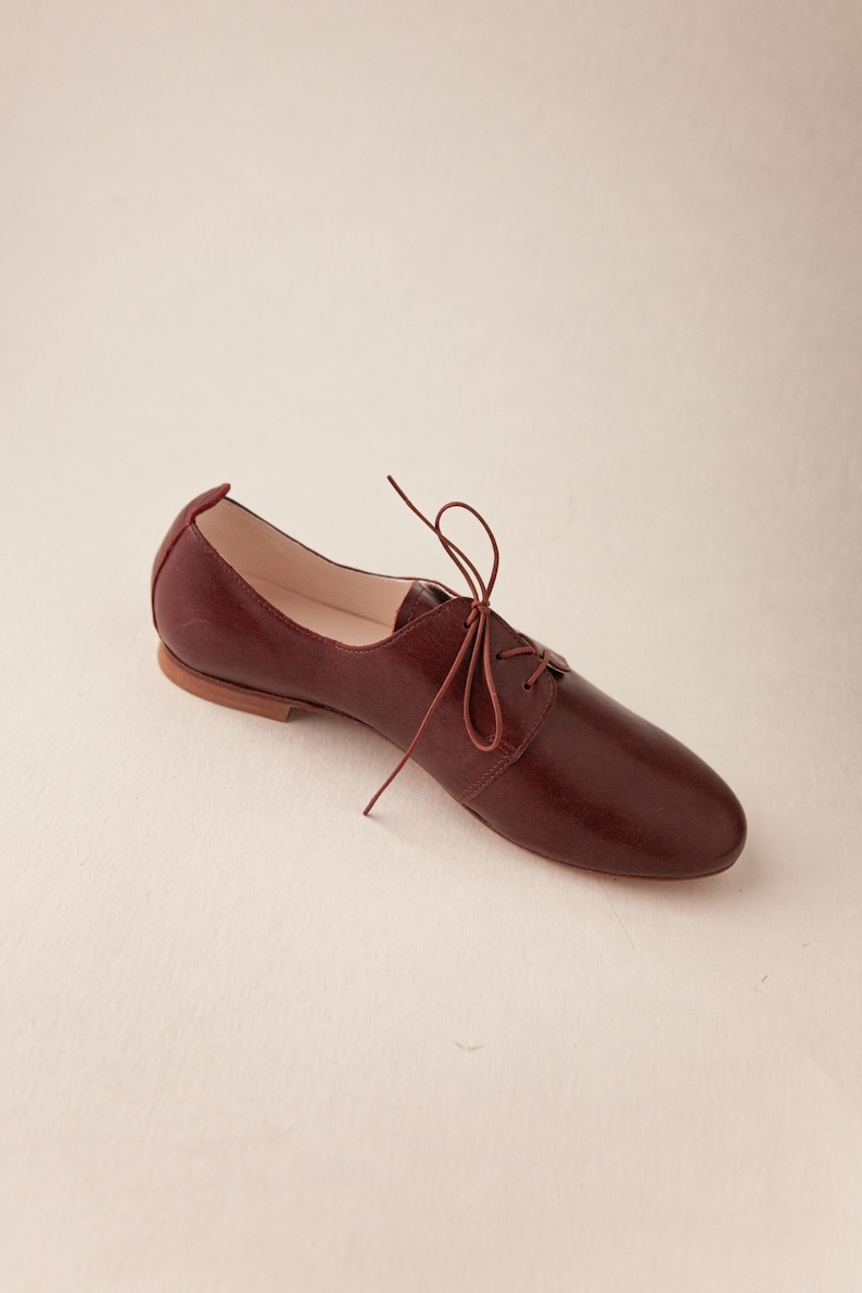 May include: A burgundy leather oxford shoe with a pointed toe and a lace-up closure. The shoe has a low heel and a smooth, polished finish. The laces are a matching burgundy color. The shoe is designed for everyday wear.