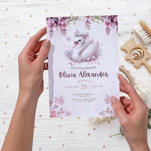 K&ouml;nnte beinhalten: Eine Babyparty-Einladung mit einem Schwan mit Krone, floralen Akzenten und dem Text "Our Little Princess Olivia Alexander". Die Einladung wird von H&auml;nden gehalten und enth&auml;lt Datum, Uhrzeit und RSVP-Informationen.