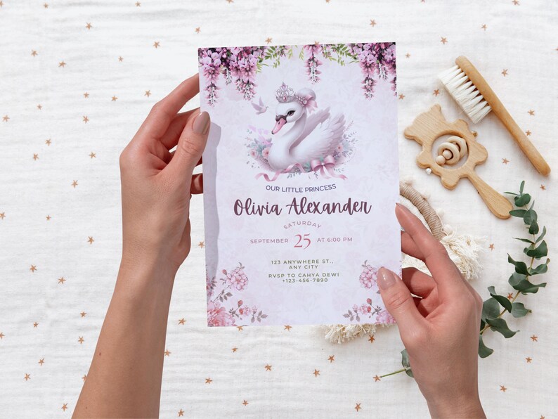 K&ouml;nnte beinhalten: Eine Babyparty-Einladung mit einem Schwan mit Krone, floralen Akzenten und dem Text "Our Little Princess Olivia Alexander". Die Einladung wird von H&auml;nden gehalten und enth&auml;lt Datum, Uhrzeit und RSVP-Informationen.