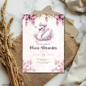 K&ouml;nnte beinhalten: Eine rosa Einladungskarte mit einer Schwan-Illustration, floralen Akzenten und dem Text "Our Little Princess Olivia Alexander". Die Karte enth&auml;lt Eventdetails: Samstag, 25. September, um 18:00 Uhr, sowie eine Adresse und RSVP-Informationen.