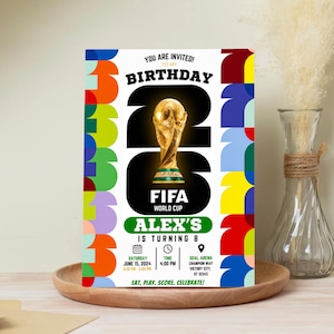 May include: A rectangular birthday invitation card featuring a large gold FIFA World Cup trophy graphic, the text "YOU ARE INVITED! TO MY BIRTHDAY", "ALEX'S IS TURNING 8", and "EAT, PLAY, SCORE, CELEBRATE!" with colorful geometric borders on the sides.