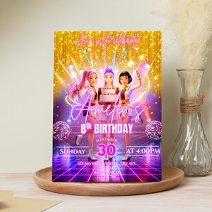 Puede incluir: Una invitaci&oacute;n de cumplea&ntilde;os con tres figuras animadas en un escenario con un fondo dorado. La invitaci&oacute;n dice "8&ordm; Cumplea&ntilde;os de Amelia" con la fecha y la hora. La invitaci&oacute;n est&aacute; en una bandeja de madera.