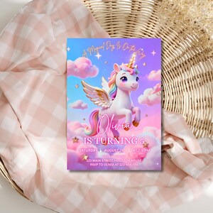 K&ouml;nnte beinhalten: Eine farbenfrohe Einladungskarte mit einem Einhorn vor einem vertr&auml;umten Himmel mit Wolken. Der Text lautet "Olivia wird 5" mit Veranstaltungsdetails. Die Karte liegt auf einem rosa-wei&szlig; karierten Stoff, auf einem Weidenkorb.