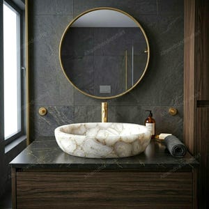 May include: A round vessel sink crafted from white and cream-colored agate stone with natural crystalline patterns. The sink is mounted on a dark marble countertop with gold veining, featuring a gold faucet and a circular mirror above it.