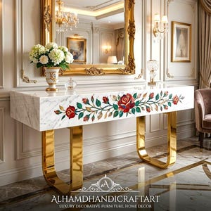 Puede incluir: Una mesa consola de mármol blanco con una incrustación horizontal de rosas rojas y hojas verdes. La mesa está sostenida por dos patas de metal dorado pulido en forma de U. El texto ALHAMDHANDICRAFTART LUXURY DECORATIVE FURNITURE, HOME DECOR es visible.