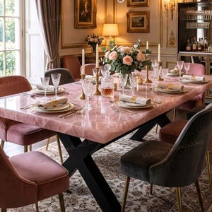Pode incluir: Uma mesa de jantar com tampo de quartzo rosa e pernas de metal preto está montada para uma refeição. Cadeiras de veludo em tons de rosa e cinza circundam a mesa. A mesa está montada com vidro, talheres e um centro floral. A mesa tem cerca de 200 cm de comprimento.