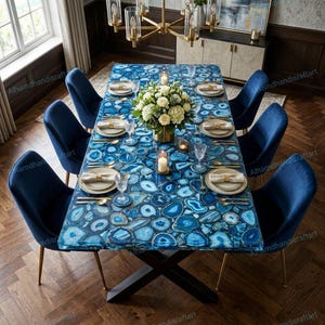 May include: A dining table with a blue agate stone top, set for a meal. The table is surrounded by six navy blue velvet chairs with gold legs. A floral centerpiece and candles adorn the table. The table's dimensions are approximately 72 inches long.