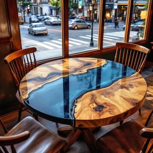 May include: Round wooden table with a blue epoxy river design. The table has a natural wood grain pattern and is supported by a wooden pedestal base. The table is surrounded by wooden chairs with brown leather seats, set in front of a window.