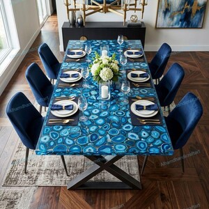 May include: A rectangular dining table with a blue agate stone top, set for a formal dinner. The table is surrounded by navy blue velvet chairs. The table setting includes white plates, gold cutlery, and wine glasses. A floral centerpiece and candles complete the elegant arrangement.