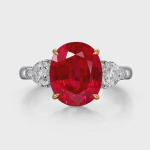 Peut inclure: Bague à trois pierres avec un grand rubis ovale, flanqué de deux diamants en forme de poire. Le rubis rouge vif est serti de griffes en or, avec un anneau en argent. Les diamants brillent.