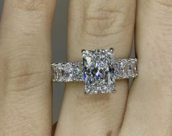 May include: A radiant-cut diamond ring with a large rectangular center stone and smaller rectangular stones on either side. The ring is set in a silver band and sparkles brightly.
