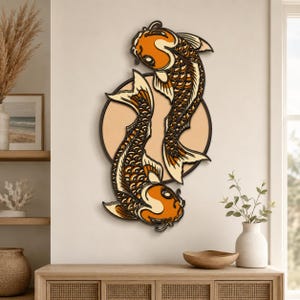 May include: A layered wooden wall art piece featuring two orange and black koi fish swimming in a circular formation. The fish are depicted with intricate scale patterns and flowing fins, set against a solid circular background in a soft beige tone.