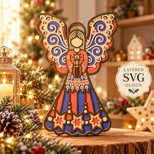 Puede incluir: Un adorno de ángel de madera multicapa con alas de volutas intrincadas, una figura central que sostiene una vela y una falda decorada con estrellas recortadas. El diseño usa tonos rojo, azul y crema, con el texto LAYERED SVG DESIGN.