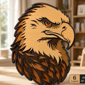 May include: A multi-layered wooden wall art piece depicting a bald eagle head in profile. The design features six distinct layers of wood in varying shades of brown and tan, creating a dimensional effect. A small rectangular label displays 6 Layers.
