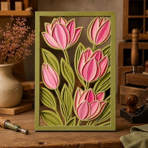 Pode incluir: Uma obra de arte em madeira em camadas com tulipas rosa e folhas verdes, emoldurada em uma moldura verde. As tulipas têm tons variados de rosa, criando um efeito 3D. A obra de arte é exibida em uma superfície de madeira.