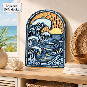 May include: A layered arched wall art piece featuring a stylized ocean wave design in shades of blue and white with a yellow sun set against a dark blue frame. The design includes the text Layered SVG design in the upper left corner.