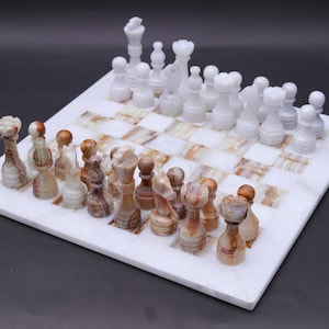 Könnte beinhalten: Ein Schachspiel aus Marmor mit weißen und braunen Figuren auf einem weiß-braun karierten Brett. Die Schachfiguren sind auf dem Brett angeordnet und spielbereit. Das Set wird auf einer dunklen Oberfläche präsentiert.