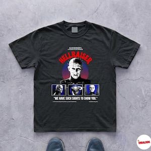 May include: Black t-shirt featuring the movie title "Hellraiser" in red letters above an image of a character with pins in their head. Below the image are three smaller images and the quote "We have such sights to show you."