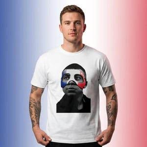 K&ouml;nnte beinhalten: Ein wei&szlig;es kurz&auml;rmeliges T-Shirt mit einem mittigen Grafikdruck einer Person, die eine Maske mit blauen, wei&szlig;en und roten Streifen tr&auml;gt. Die Person auf dem Bild ist in Schwarz-Wei&szlig; gehalten, w&auml;hrend die Maske farbig dargestellt ist.