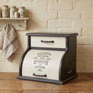 以下が含まれることがあります： 黒とクリーム色のパン箱。引き出しと湾曲した前面が付いています。ボックスは使い古された仕上げで、「KITCHENS ARE MADE FOR FAMILIES TO GATHER」というテキストが前面に印刷されています。2つの黒いハンドルがあります。