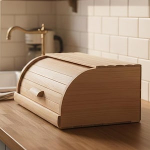 Puede incluir: Una panera de madera clara con tapa enrollable y frente curvo. La panera tiene un pequeño asa y está sobre una encimera de madera en una cocina. La panera está hecha de madera clara.