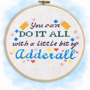 May include: Cross-stitch embroidery in a wooden hoop. The text reads "You can DO IT ALL with a little bit of Adderall" in various colors. Decorative elements include stars, hearts, and geometric shapes.