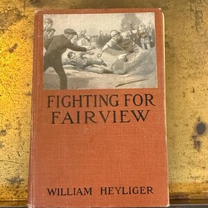 May include: A hardcover book titled Fighting for Fairview by William Heyliger with a rust-colored fabric cover. The front cover features a black and white illustration of a baseball game in progress, showing players sliding into a base.