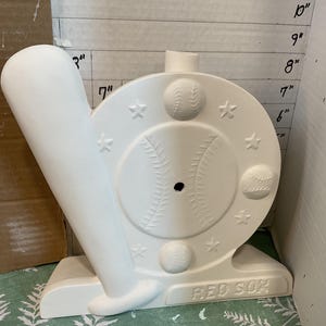 May include: White ceramic baseball themed figurine with a baseball bat and a wheel with baseballs and stars. The base of the figurine says "RED SOX".