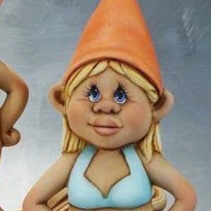 May include: A ceramic garden gnome figurine of a woman wearing a light blue bikini and orange hat. The gnome has blonde hair, blue eyes, and is wearing white sandals. The figurine is standing with hands on hips.