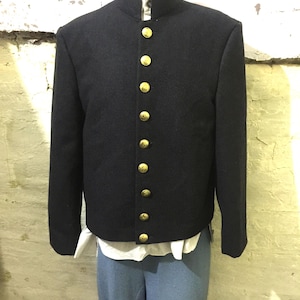 May include: A dark navy blue jacket with a mandarin collar and gold-colored buttons. The jacket is part of a uniform, paired with light blue pants and a white shirt. The jacket has a tailored fit and a classic design.